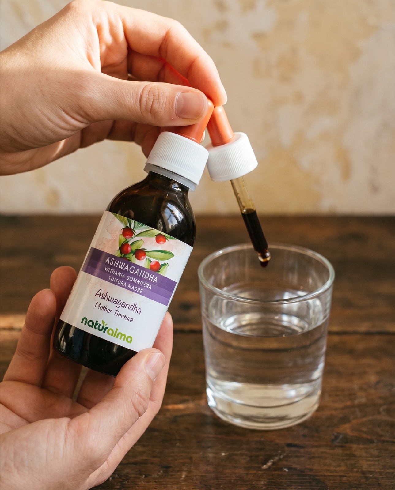 Ashwagandha estratto idroalcolico — gocce versate da un contagocce in un bicchiere d'acqua, radice e bacche rosse di ashwagandha
